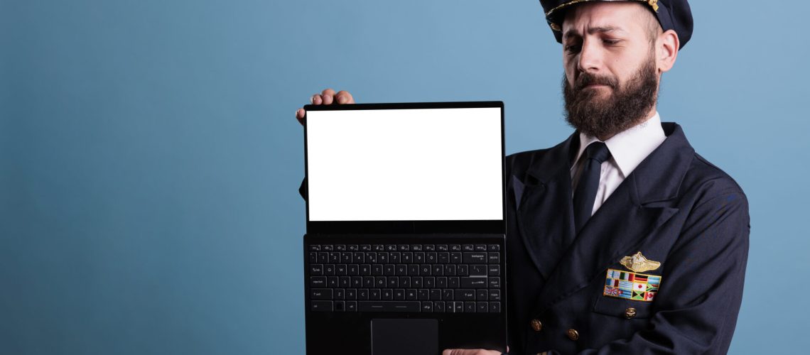Serious airplane pilot showing laptop with empty white screen, aviation academy software advertising, pc with airport website mockup. Plane captain holding portable computer with blank display